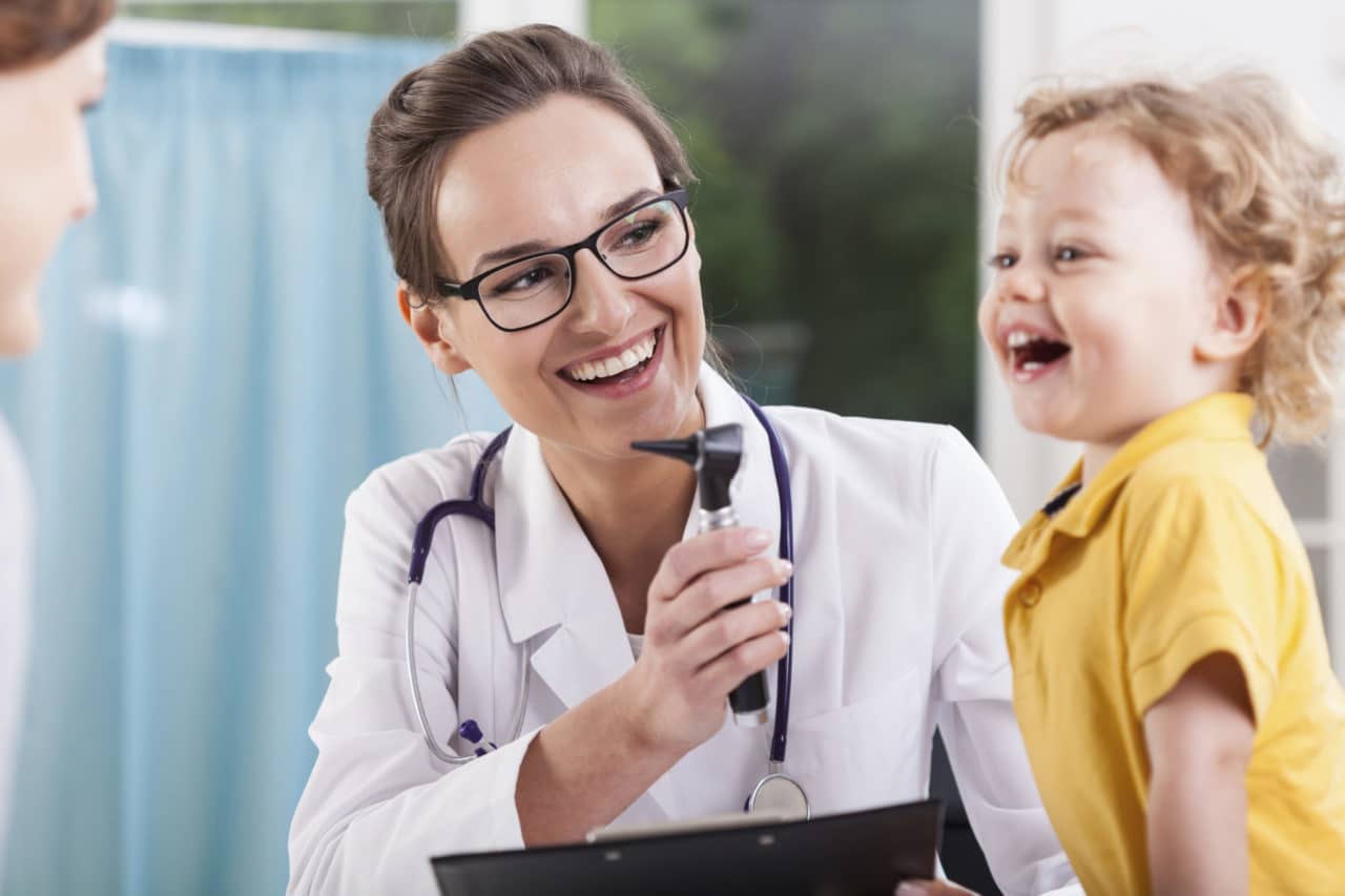 Photo of an audiologist holding an otoscope near a laughing child