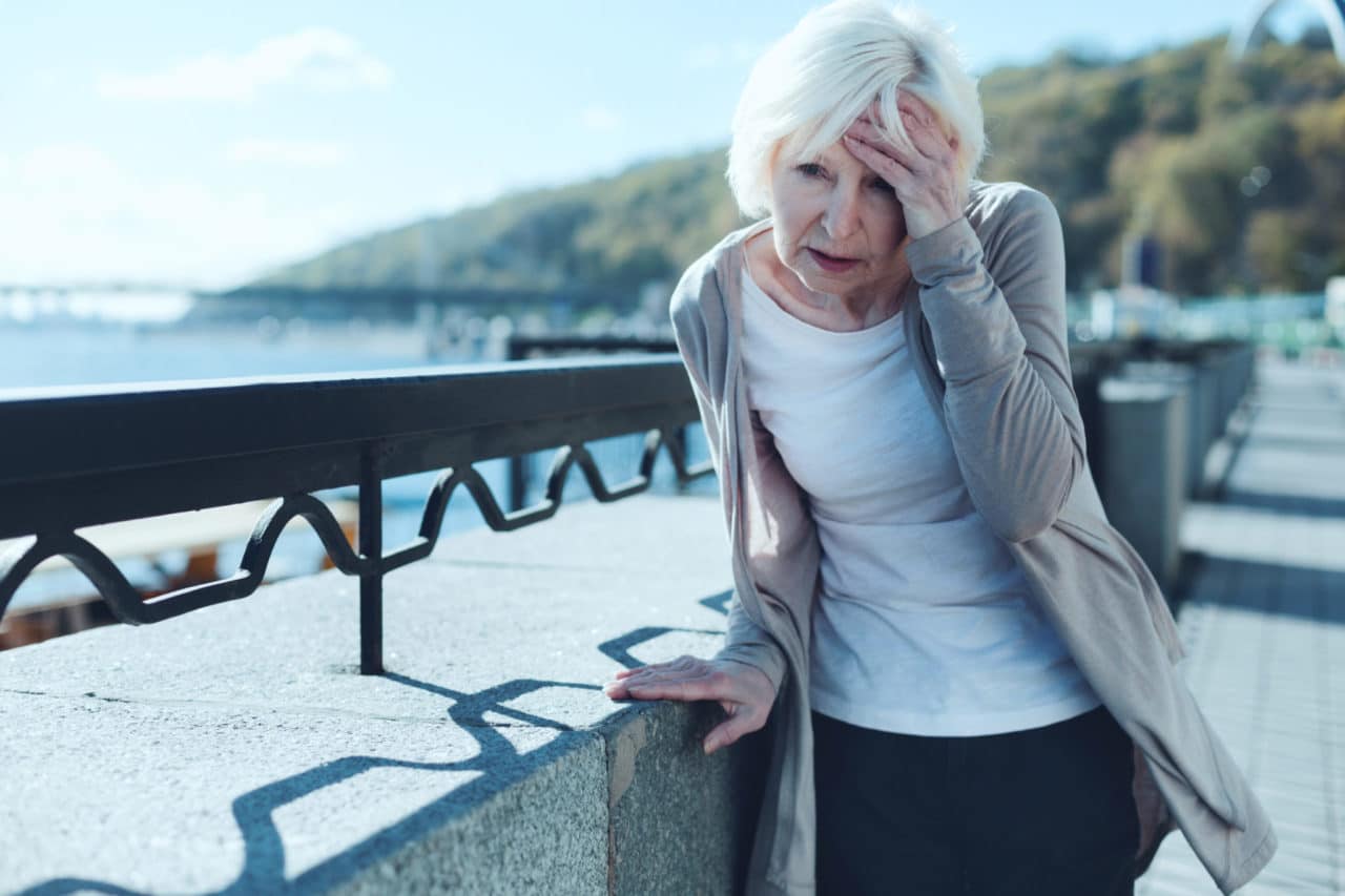 Photo of a person standing on a bridge, leaning against the support and clutching their head in pain