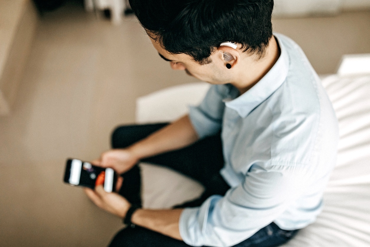 Man with hearing aids looking at phone in hotel room