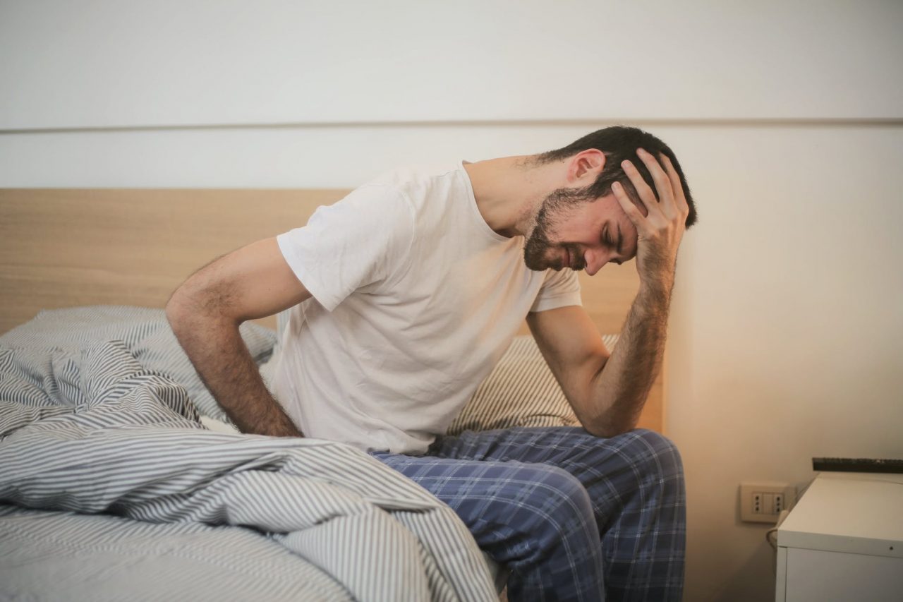 Man sits on edge of bed with headache.