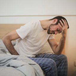 Man sits on edge of bed with headache.