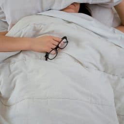 Woman sleeping and holding glasses in bed.
