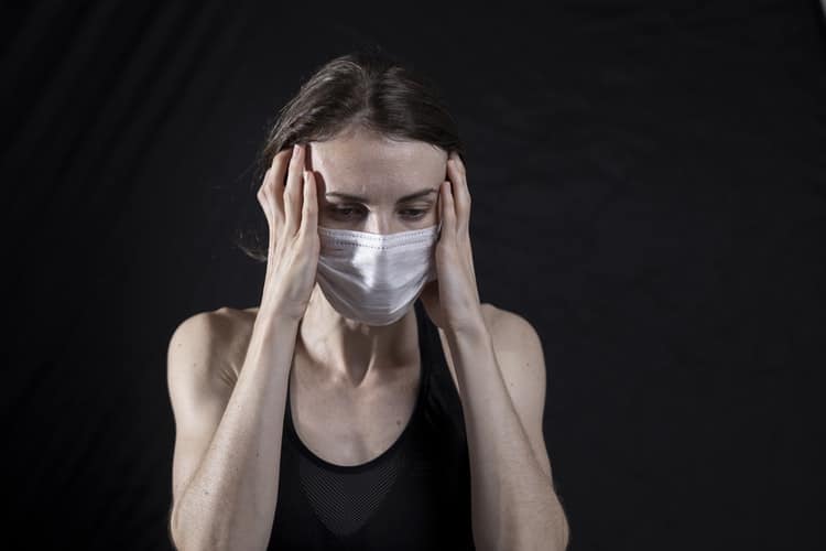 Woman with a headache wearing a mask.