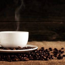 A white cup of coffee surrounded by coffee beans.