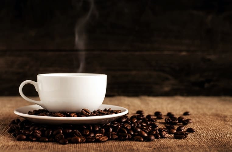 A white cup of coffee surrounded by coffee beans.