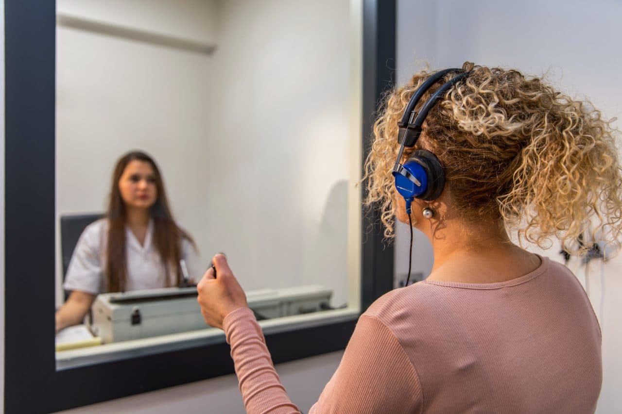 An audiologist gives a hearing test in a sound booth.