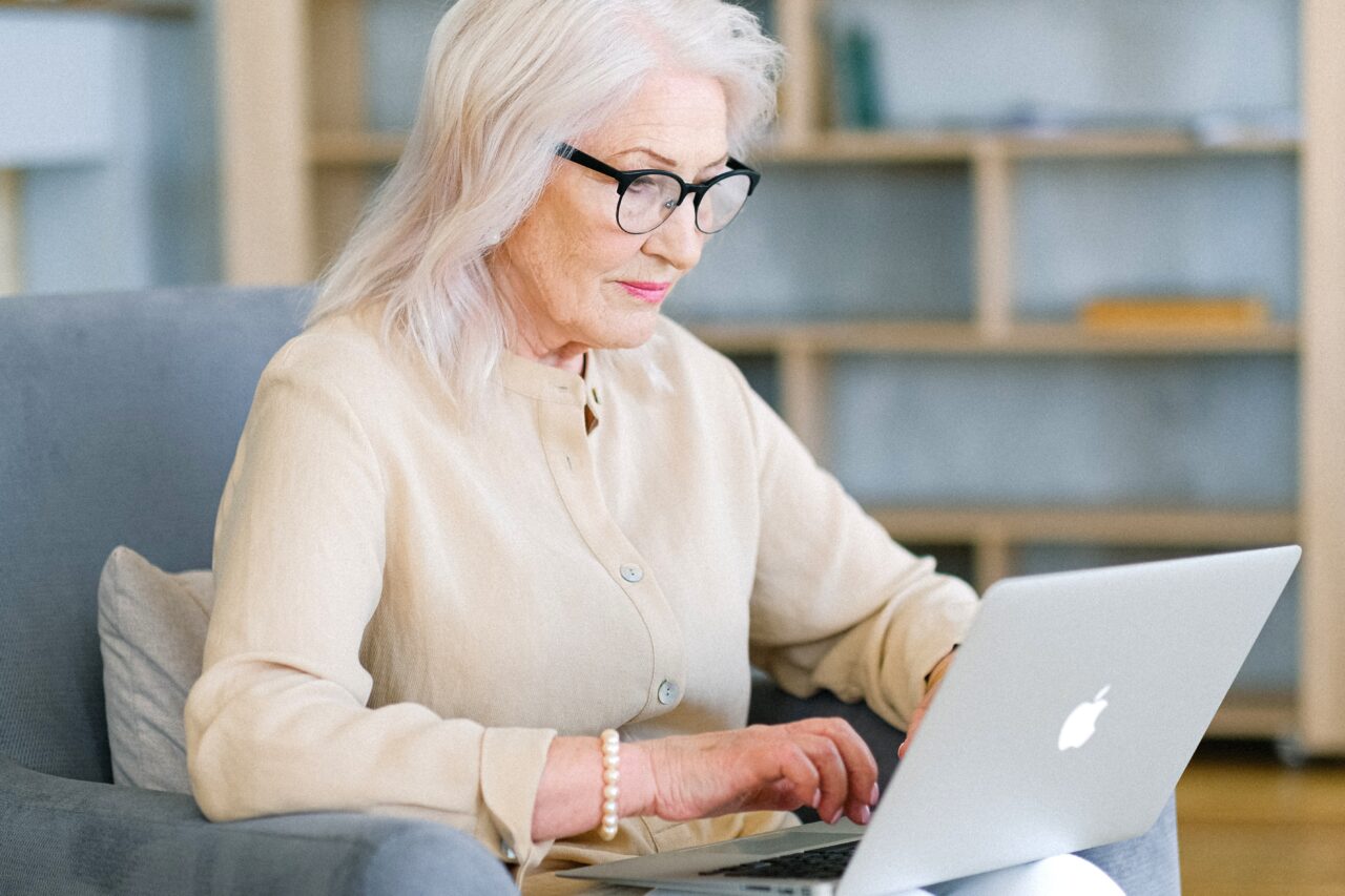 Older woman with glasses working on her laptop.