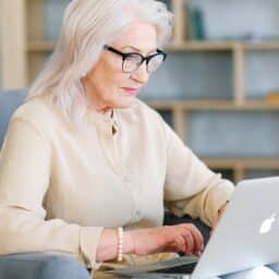 Older woman with glasses working on her laptop.