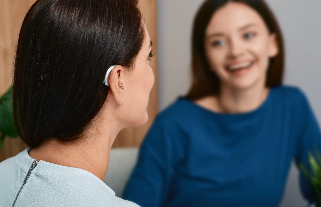 Young woman with a hearing aid talking with her friend.