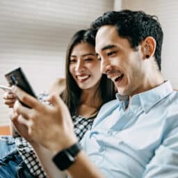 Man wearing hearing aid sitting on a couch with his girlfriend looking at his phone