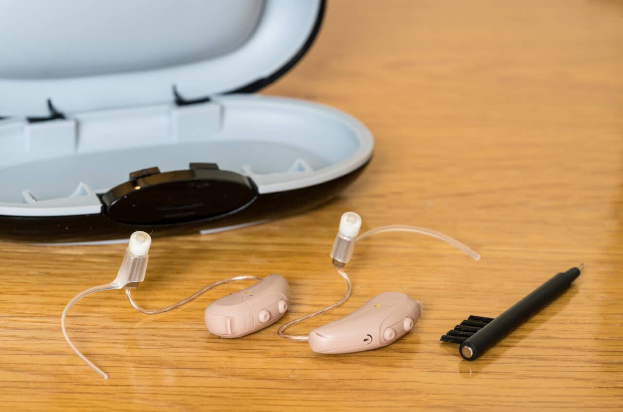 Close up of a pair of tiny modern hearing aids and a cleaning brush on bedside table.