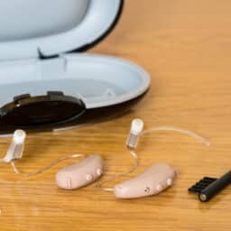 Close up of a pair of tiny modern hearing aids and a cleaning brush on bedside table.