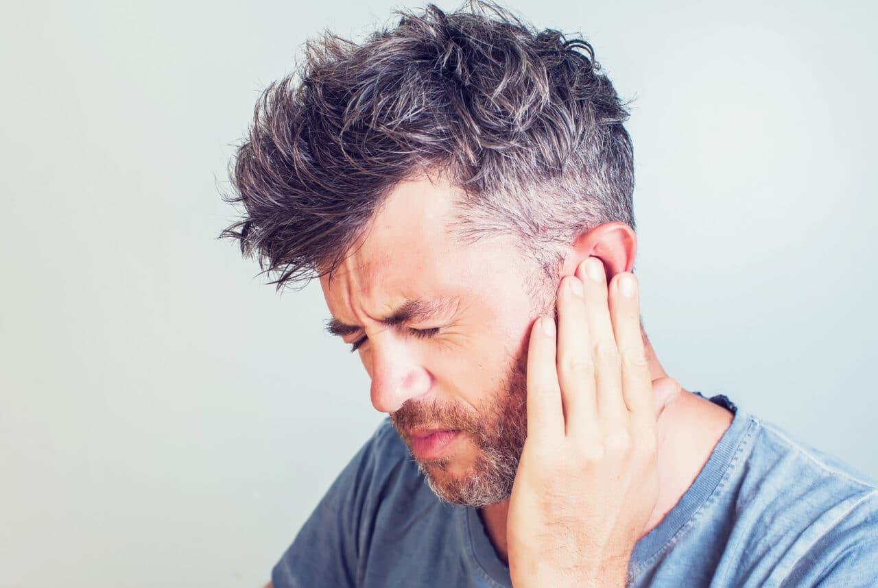 Man with tinnitus pressing his hand to his ear.