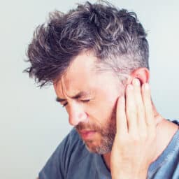 Man with tinnitus pressing his hand to his ear.