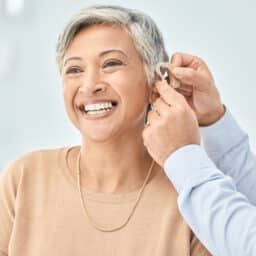 Audiologist putting a hearing aid on a happy woman.