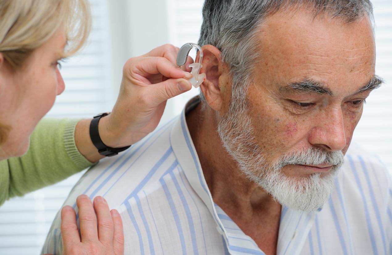 Audiologist positioning a man's hearing aid.