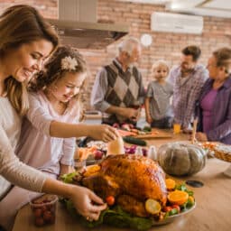 Mom and daughter putting the finishing touches on a turkey with family in the background