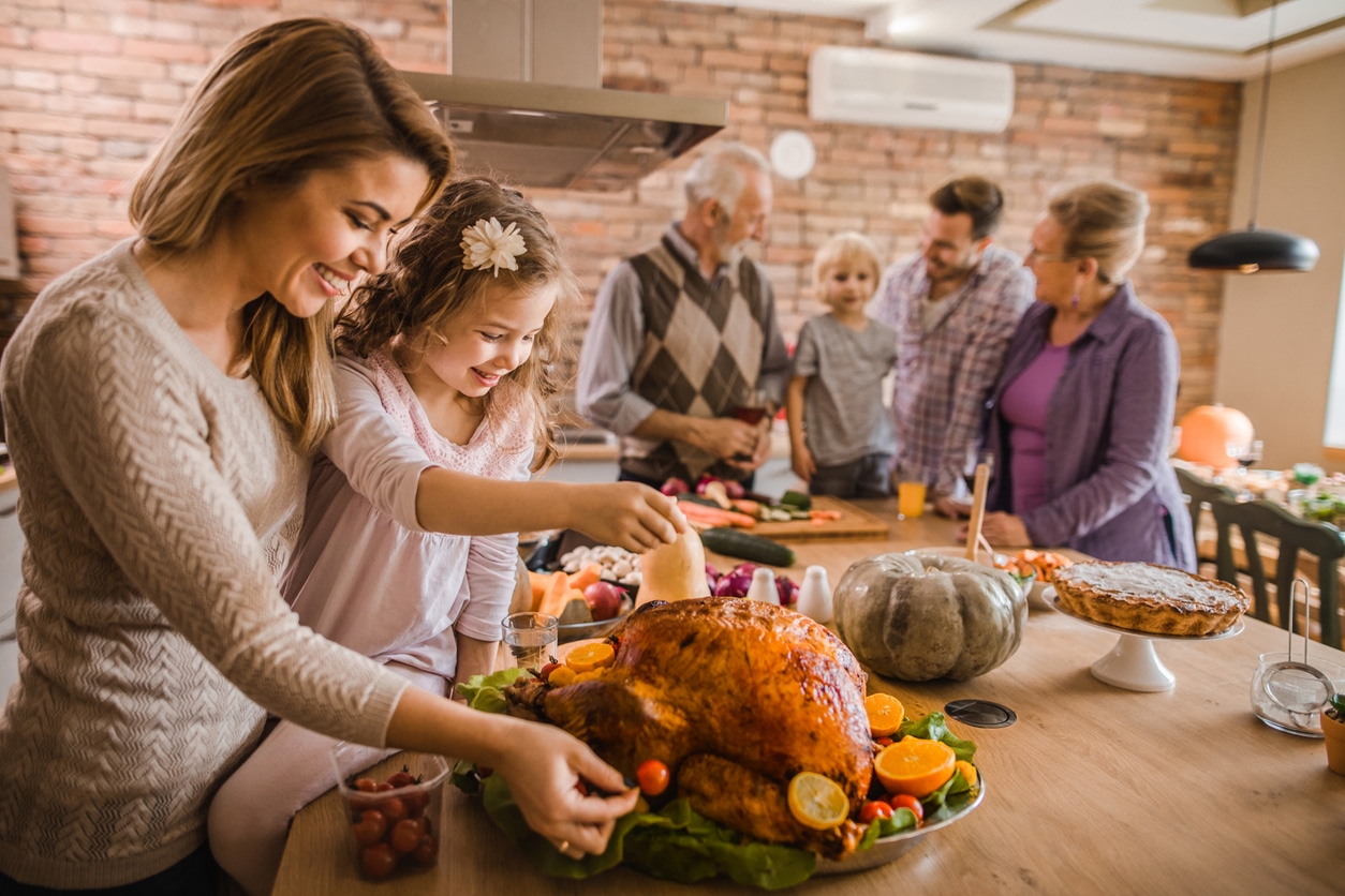 Mom and daughter putting the finishing touches on a turkey with family in the background.