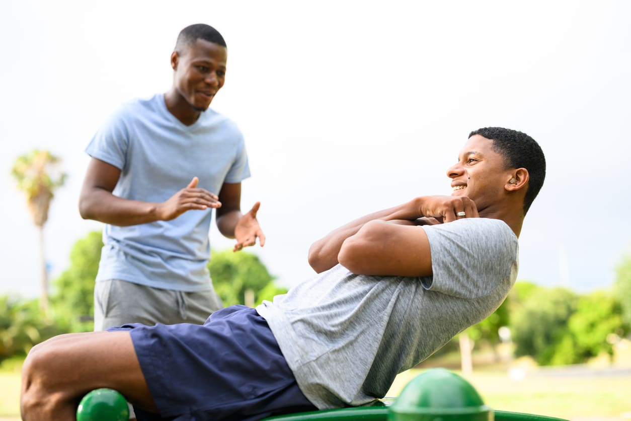 Young man wearing hearing aid doing sit ups on sports equipment in park.