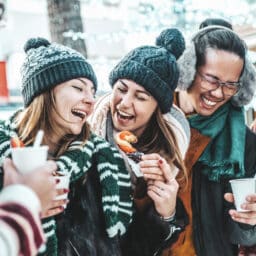 Laughing friends drinking hot chocolate at the winter market