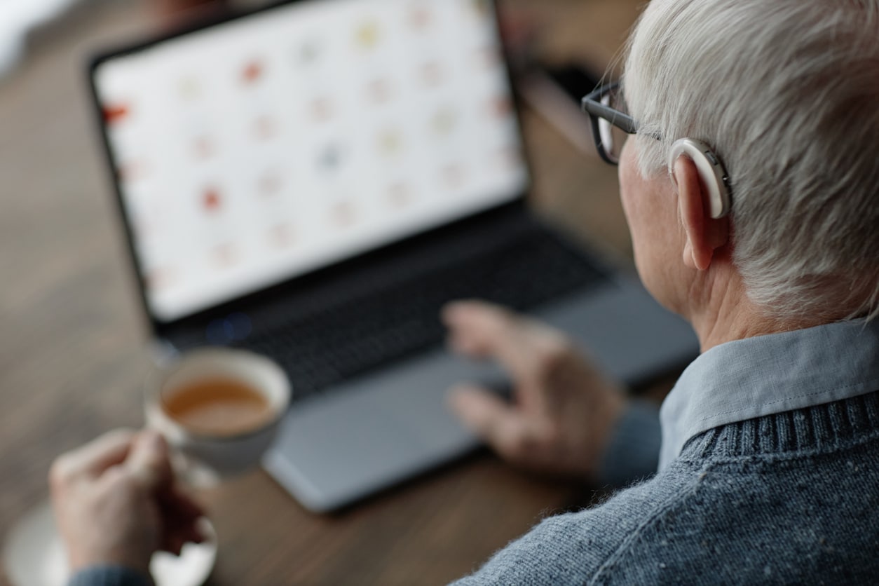 Senior Man Wearing Hearing Aid Working on Laptop at Home
