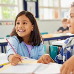 Happy smiling school girl helping classmate in classroom