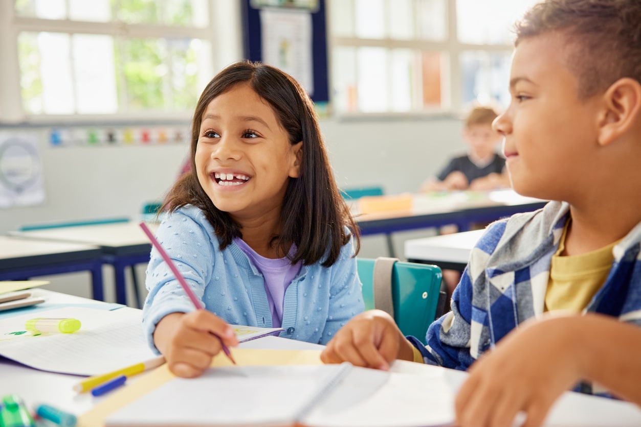 Happy smiling school girl helping classmate in classroom 