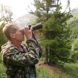 Man in camo looking through binoculars in the woods