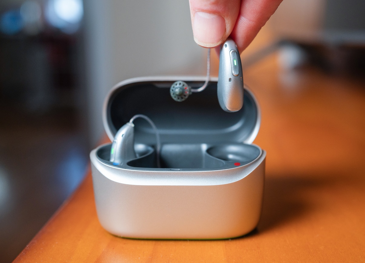 Hand holding hearing aid over charging case on table